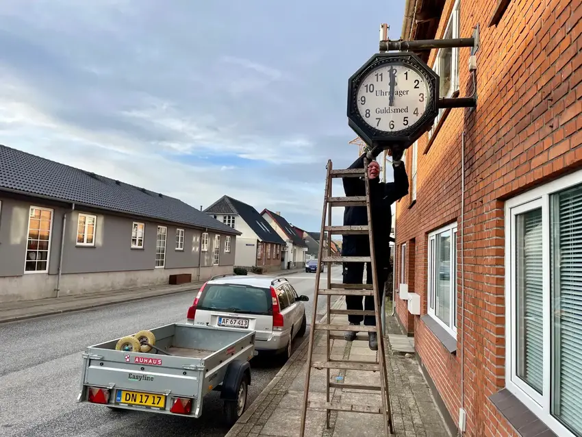 Mand på stige stiller et stort ur til klokken 12