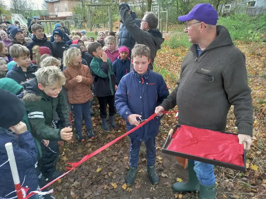 Mand med grøn jakke og hat står sammen med mange børn